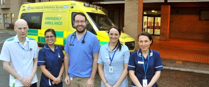 A mix of clinical staff standing in front of an ambulance smiling.