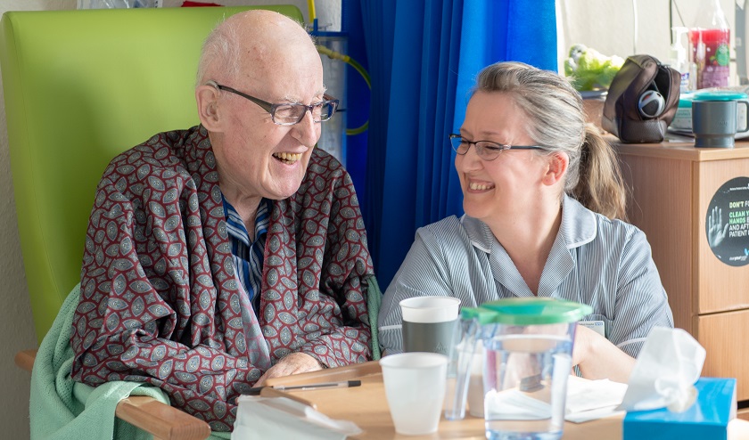 Female nurse sat with male patient, they are both laughing