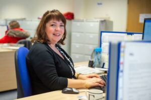 A non-clinical employee sat at a desk smiling at the camera