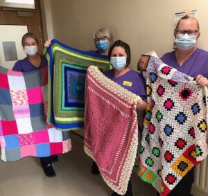 Dementia Care Team holding donated knitted blankets for patients