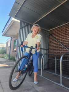 Julia Clarke, Director of Public Participation astride a bike outside the new bike rack at William Farr House. 