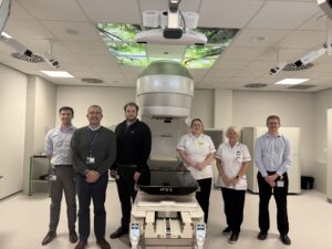 Matty Barnett, Trainee Physicist, Dr Rick Sims, Callum MacMillan, Radiotherapy Engineer, Jayne Matthews, Therapeutic Radiographer, Amanda Welsh, Chief Dosimetrist,and Daniel Kelly, Physicist, with the LINAC Machine and new cameras in the foreground
